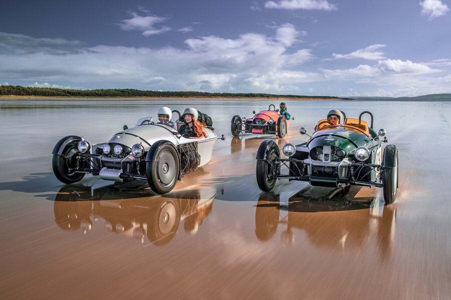 Three Morgan Super 3 cars race through the water on a beach