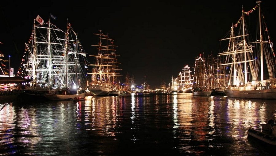 Tall ships with their masts and spars lit up at night at the L'Armada quaysides in Rouen