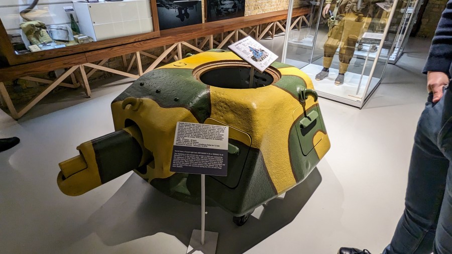 A small brown and green camouflaged tank turret sits on the Dynamo Museum floor.
