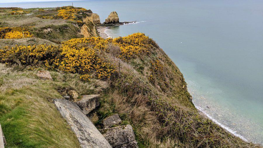 A view along the cliff with grass and yellow gorse, down to the beach and a promontory in the distance