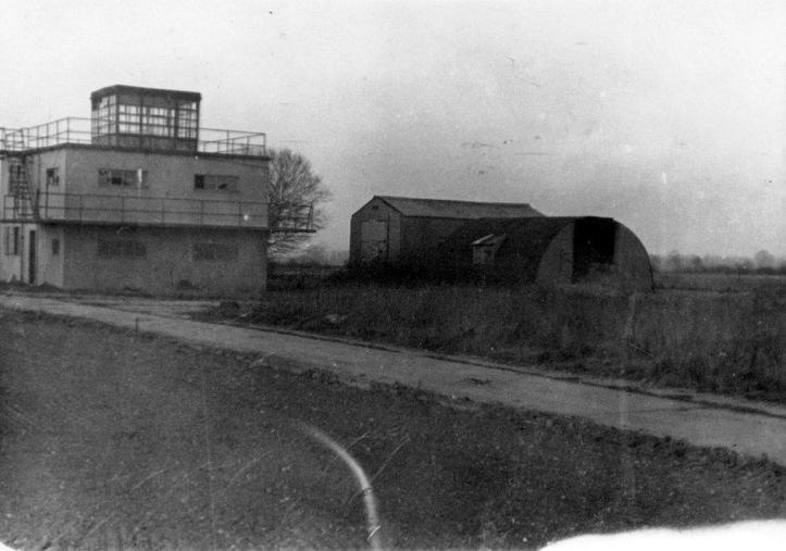 Grainy black & white photo of a control tower and some huts nearby