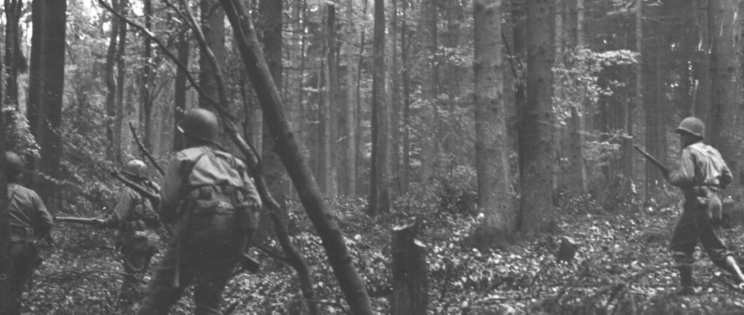 Black & white photograph of US infantrymen walking through dense woodland