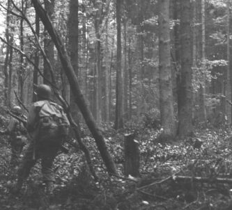 Black & white photograph of US infantrymen walking through dense woodland