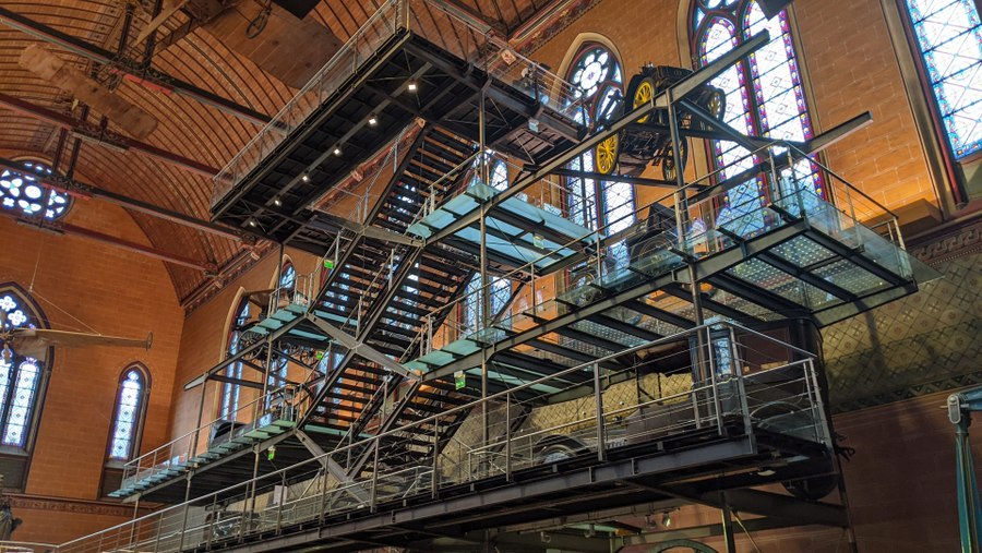 A steel network of stairs and platforms with vehicles on display, climb upward in the spacious church nave.