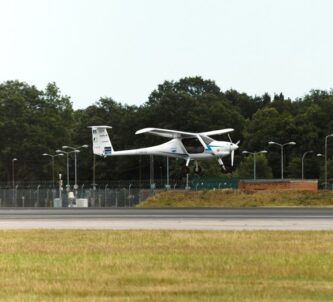 A small and slender light aircraft landing on a large runway