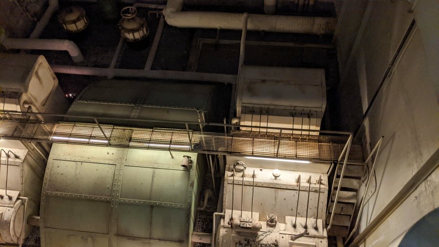 Grey metal generators at the bottom of a tall engineering compartment with metal staircases