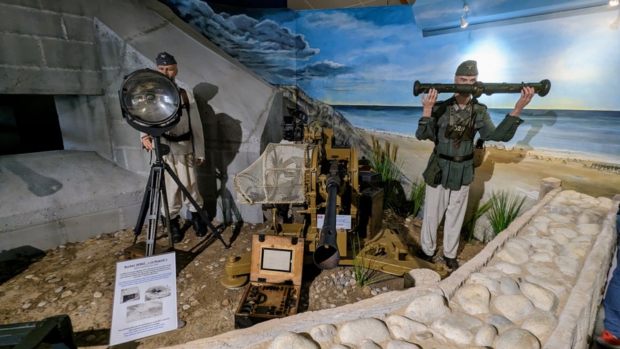 Diorama. German soldiers stand outside a recreation of the Wn 65 bunker, with range-finders and a searchlight