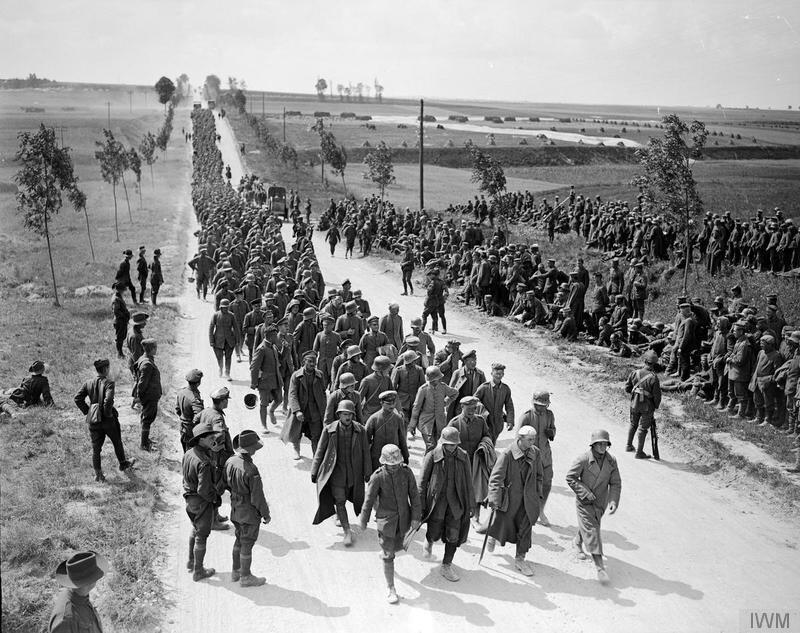 A column of german prisoners of war marching on a long straight road while allied soldiers (Australians) look on