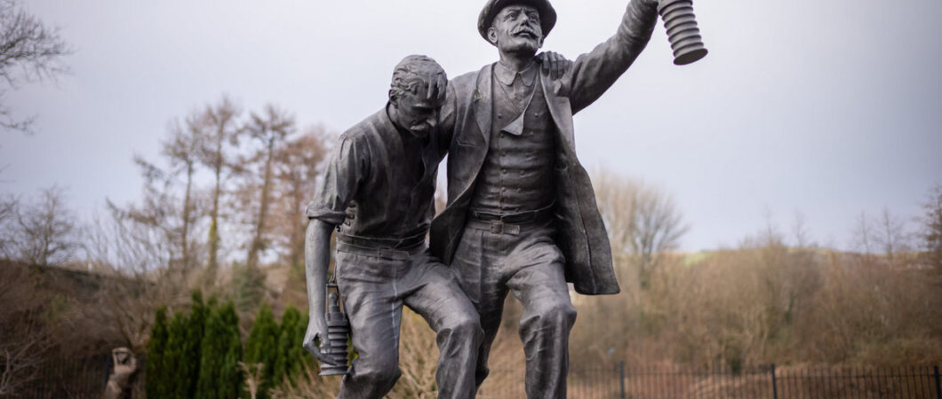 Statue on a plinth of a man holding a lantern helping an injury miner to safety