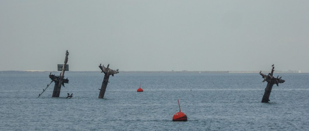 Three T-shaped masts stick out of the sea with a red warning buoy in the foreground