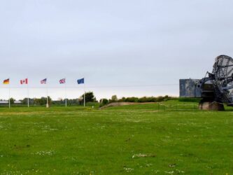 A large radar dish with the top of a bunker beside it and a row of national flags
