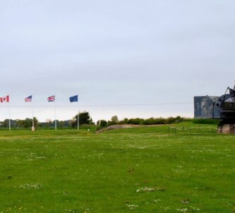 A large radar dish with the top of a bunker beside it and a row of national flags