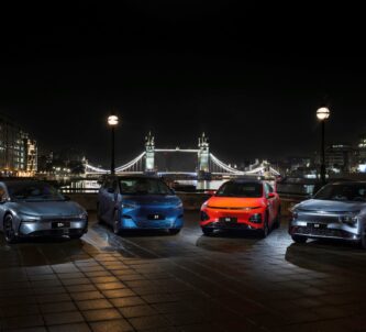 A set of fours electric cars are displayed at night in London with Tower bridge in the background