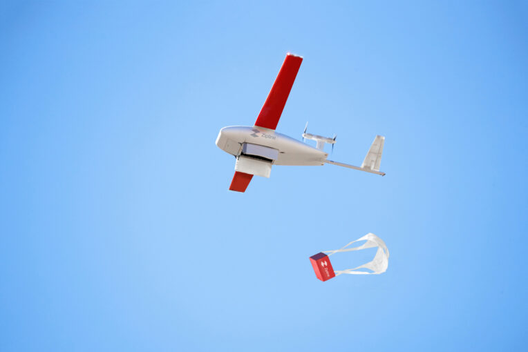 A small red winged electric UAV drops a package by parachute