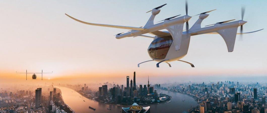 Artist's rendition: A futuristic white helicopter shaped aircraft descends towards a modern city at dusk