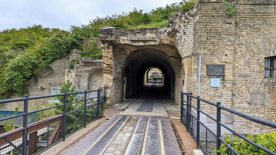 A stone bridge over the moat leading to the slightly damaged entrance to a long tunnel