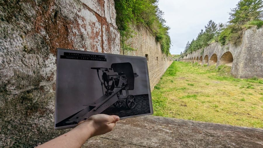 A photo is held up to show a gatling gun in this location