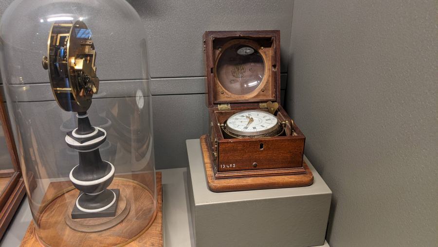 A clock in a large glass cloche, and next to it a gimballed marine clock in a wooden box
