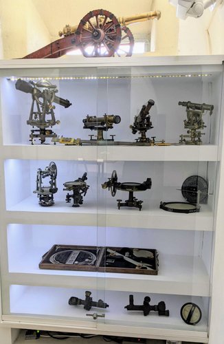 A white display cabinet with theodolites and sighting equipment displayed in it