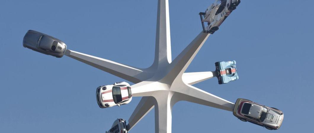 Six classic Porsche cars on spikes against a blue sky
