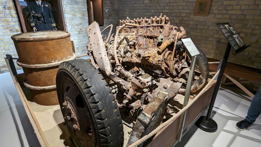 A piece of wreckage on display; the rusty engine and front wheels