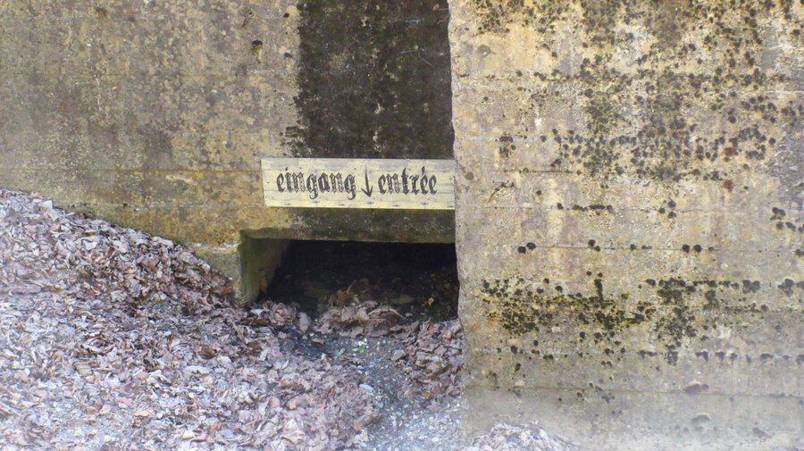 Rubble fills a doorway almost to the top. Above it in gothic script the words "eingang / entrée" are painted